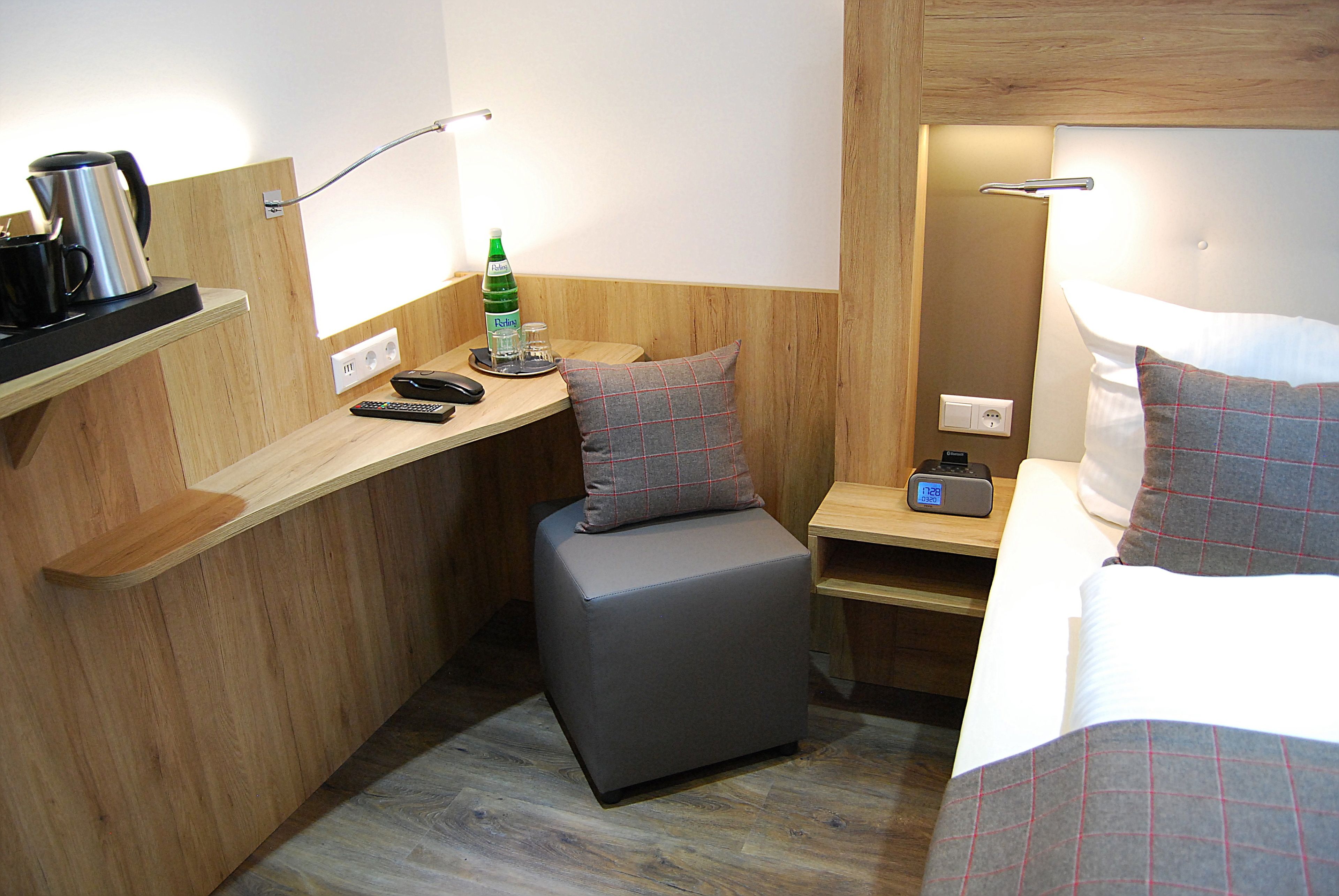 Ein kleines Hotelzimmer mit einem Bett, einem Schreibtisch, einem Stuhl, einem Nachttisch und einer Nachttischlampe.