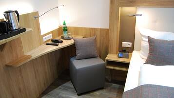 Ein kleines Hotelzimmer mit einem Bett, einem Schreibtisch, einem Stuhl, einem Nachttisch und einer Nachttischlampe.