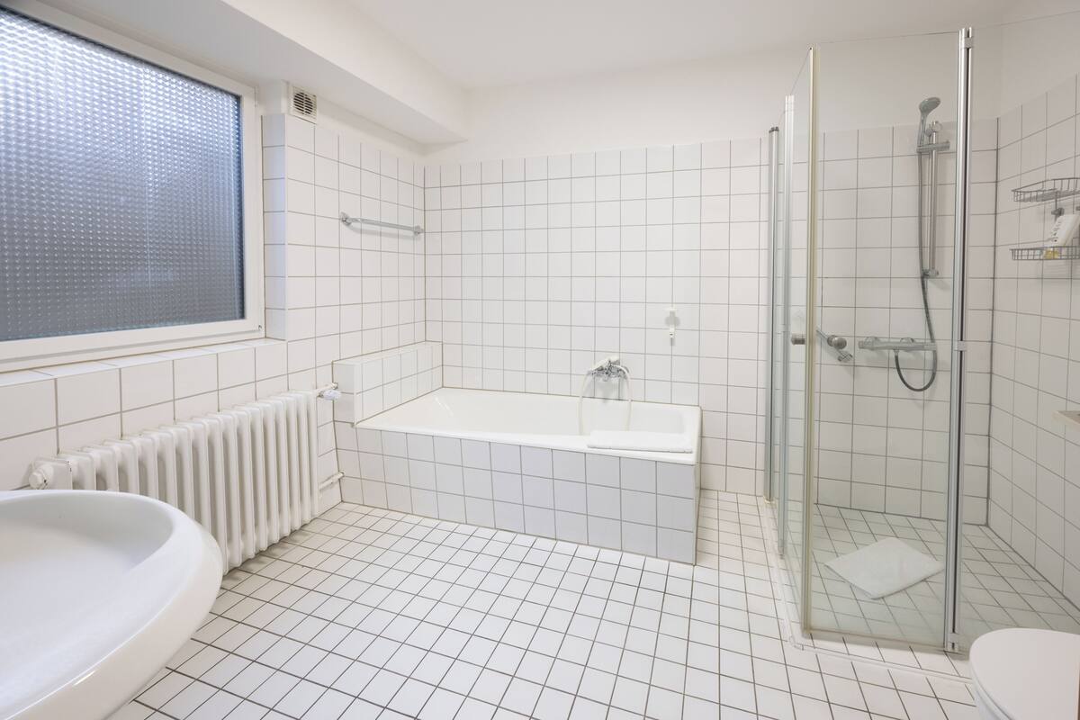 Een badkamer met een bad, een douche, een toilet en een raam.
