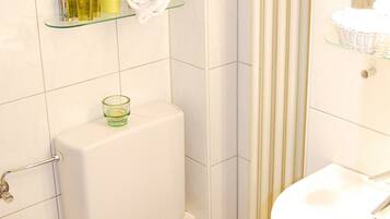 Ein Badezimmer mit Toilette, einer Glasablage für Pflegeutensilien und einer Duschvorhang.