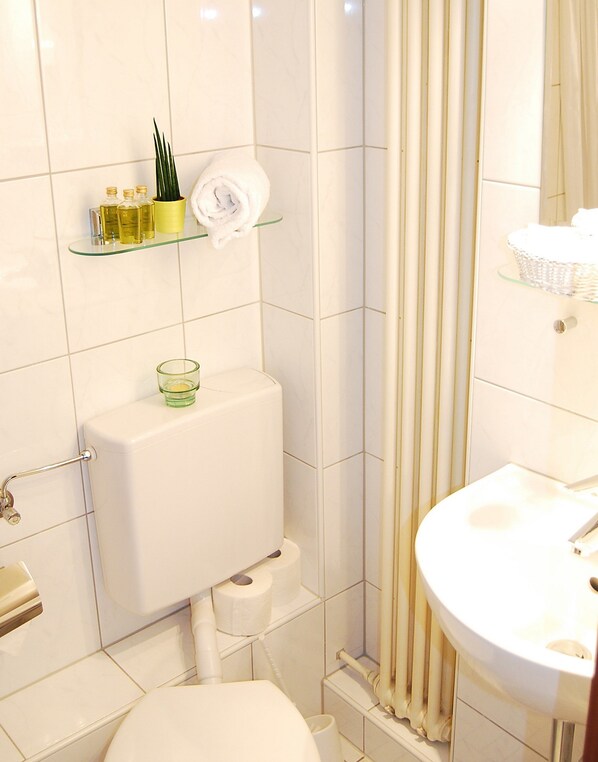 Un baño con inodoro, una repisa de vidrio con artículos de aseo y una cortina de ducha.