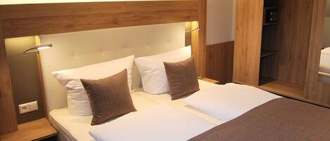Una cama doble con almohadas blancas y de cuadros, un cabecero de madera y mesitas de noche.
