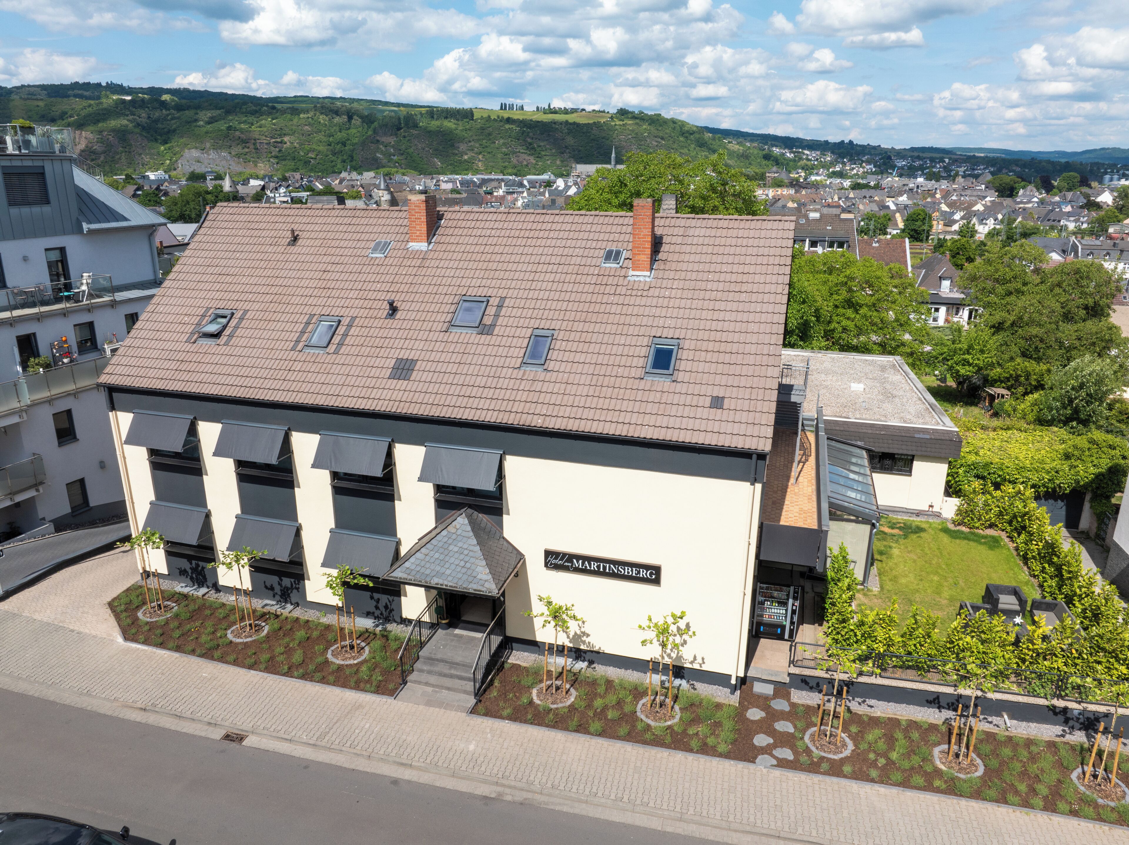 A hotel with a tiled roof, a sign reading 'Hotel Martinsberg,' and a landscaped front yard with young trees.