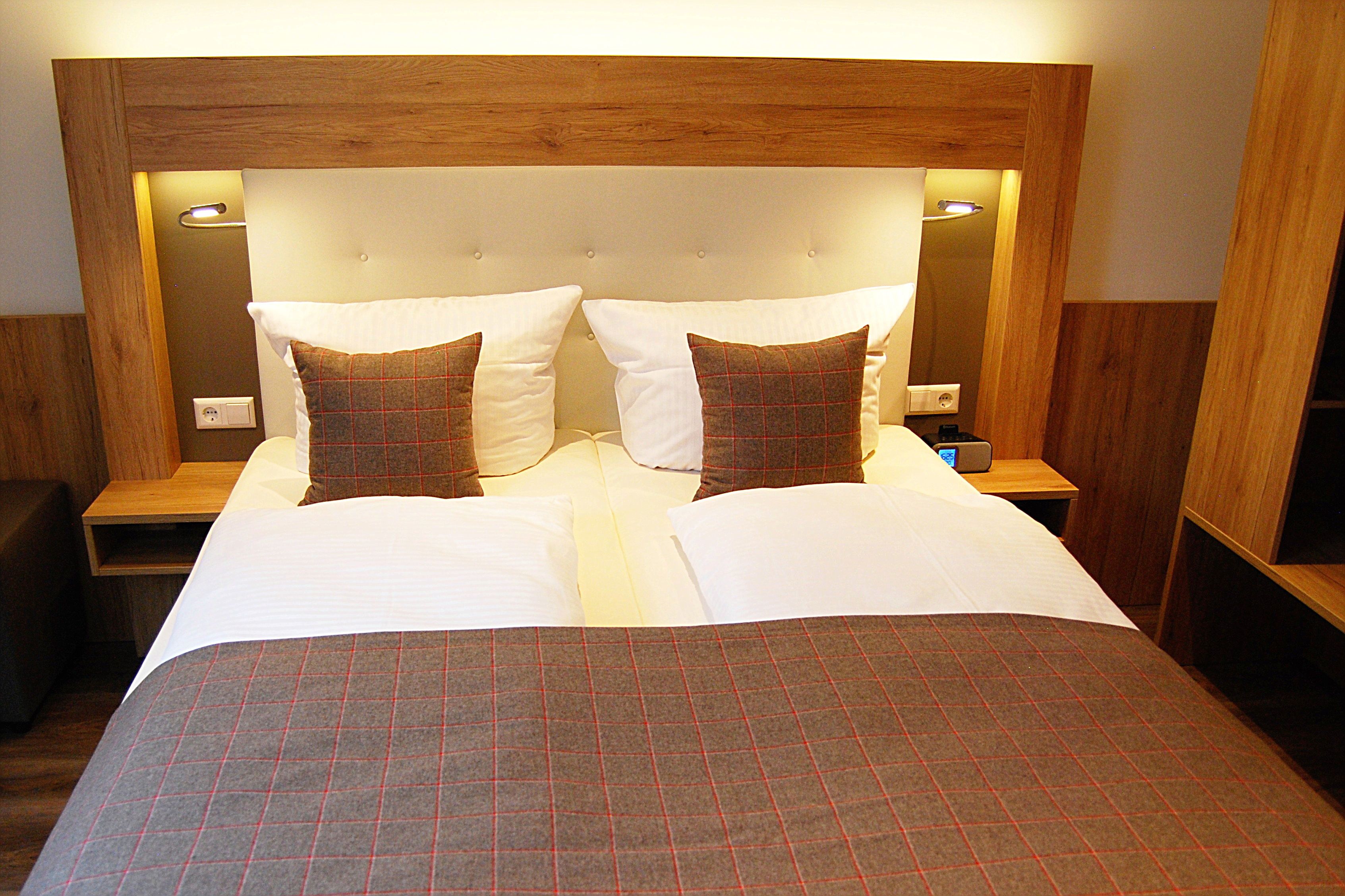 A double bed with a plaid bedspread, two white pillows, and a wooden headboard with integrated lighting.