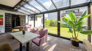 Un intérieur moderne avec un plafond en verre, un coin repas avec des chaises roses et une grande plante en pot.