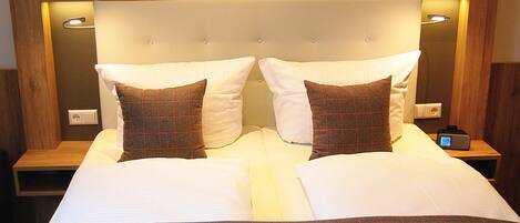 A double bed with a wooden headboard, two bedside tables, and a digital clock.