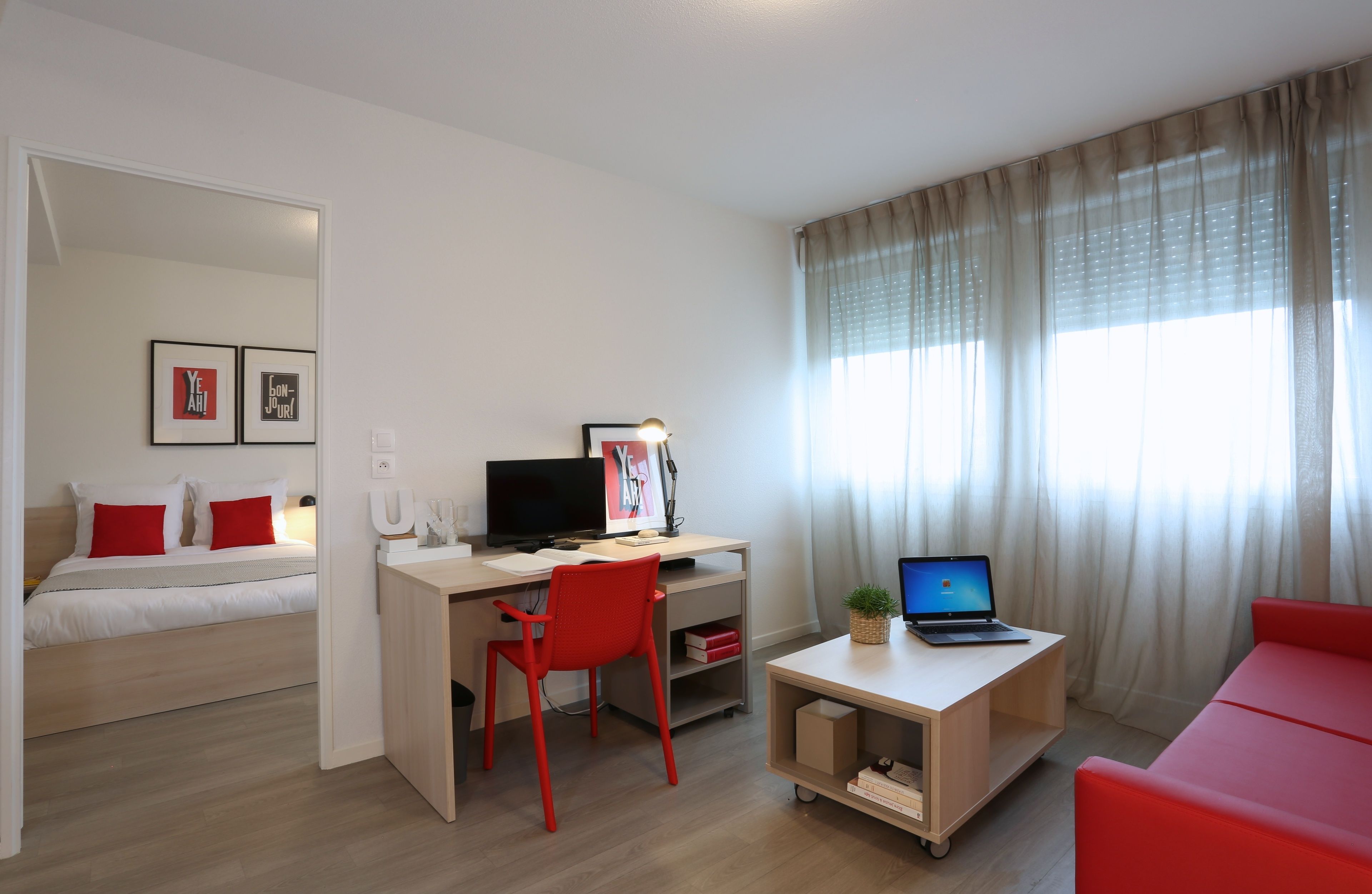 Una habitación de hotel moderna con una cama, un escritorio con un ordenador portátil, una silla roja y un sofá rojo.