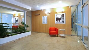 A modern lobby with a wooden wall, a red chair, a small table, and a plant. - Apparteo Nancy (Nancy)