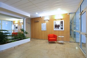 A modern lobby with a wooden wall, a red chair, a small table, and a plant.