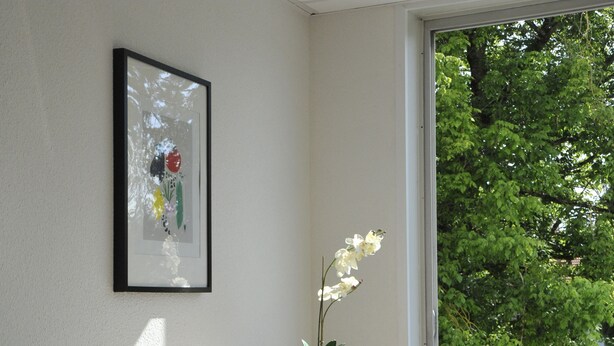 A modern room with a large window, a framed artwork on the wall, a potted plant, and two red bar stools. - Apparteo Nancy (Nancy)