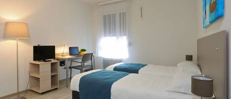 A hotel room with two beds, a desk with a computer, a chair, and a lamp.