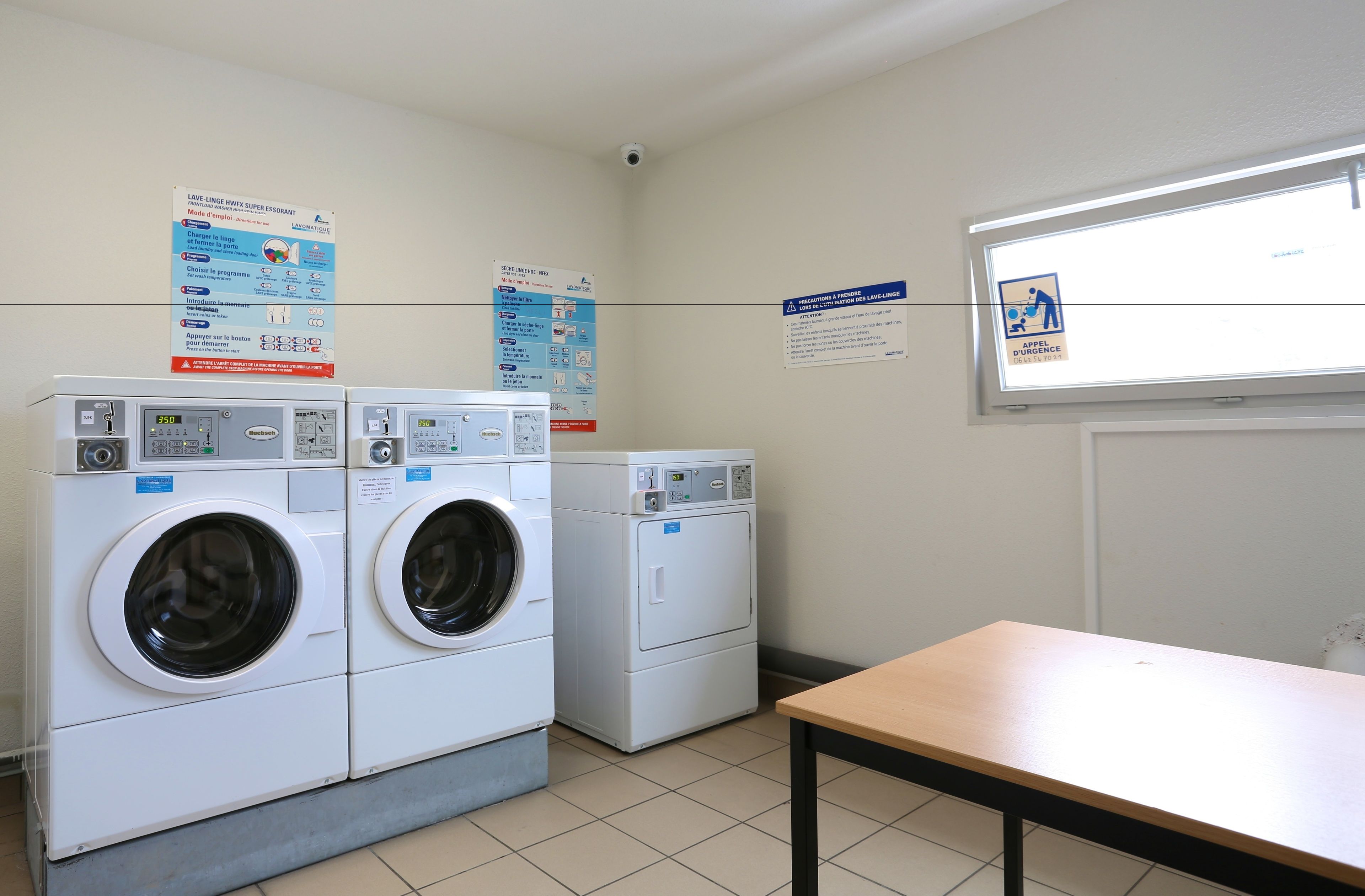 A laundry room with two front-loading washing machines, a table, and informational posters on the walls.
