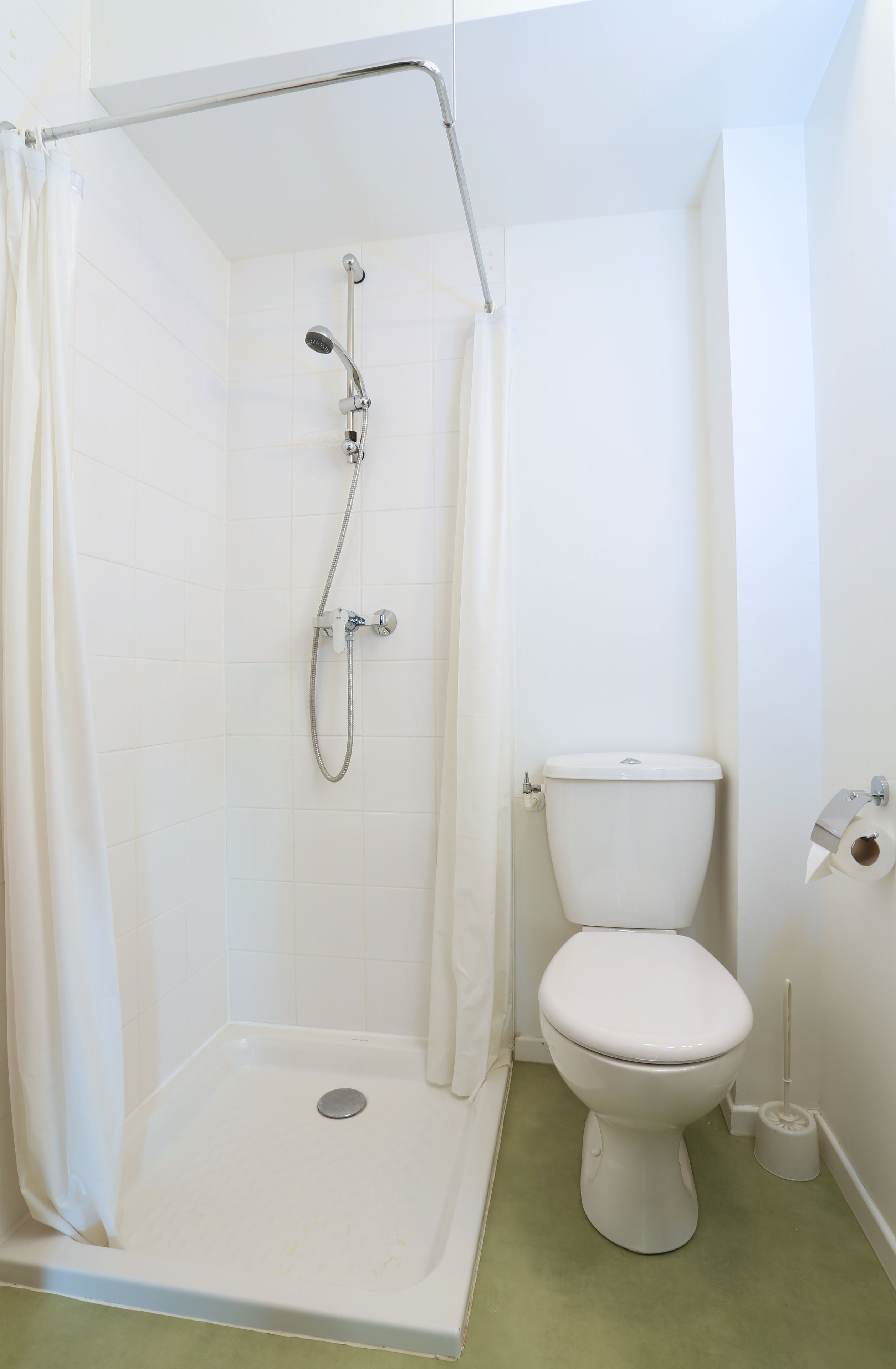 Ein Badezimmer mit Dusche, Toilette und einer Toilettenpapierrolle an der Wand.