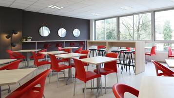 A classroom with red chairs and tables, large windows, and a dark wall with mirrors.