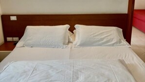 A neatly made bed with white linens, a wooden headboard, and a wall-mounted light fixture above it.