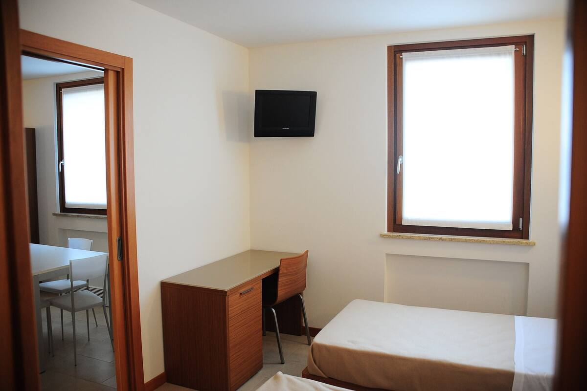 A small, clean room with a bed, a desk, and a TV.