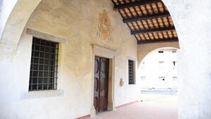 An arched doorway with a wooden door, a window with metal bars, and a patterned ceiling.