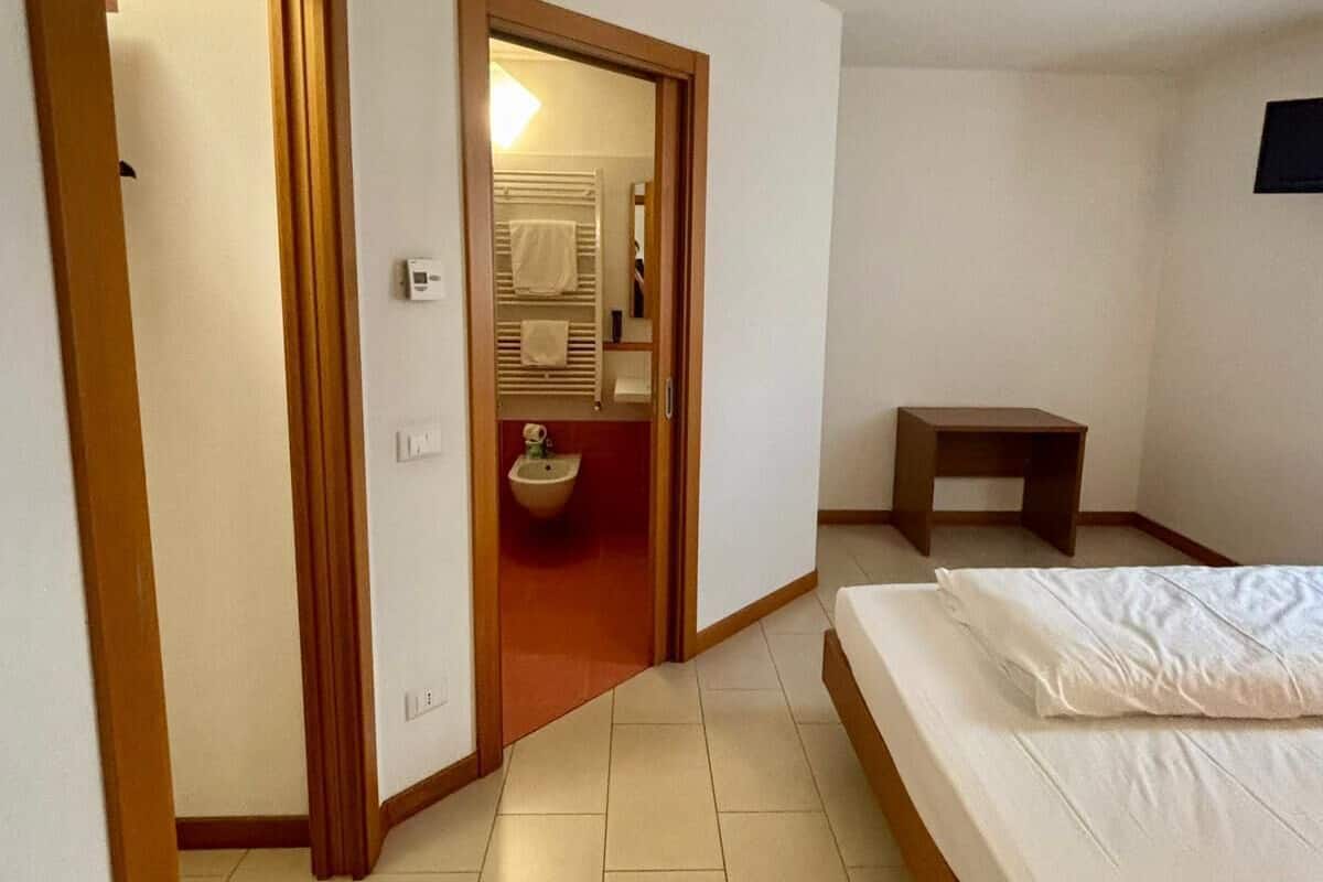A hotel room with a bed, a small table, a bathroom with a sink and towel rack, and a door leading to another room.