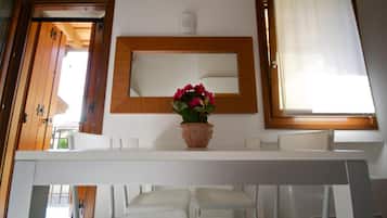 A room with a white table, a potted plant, a mirror, and a window with a curtain.