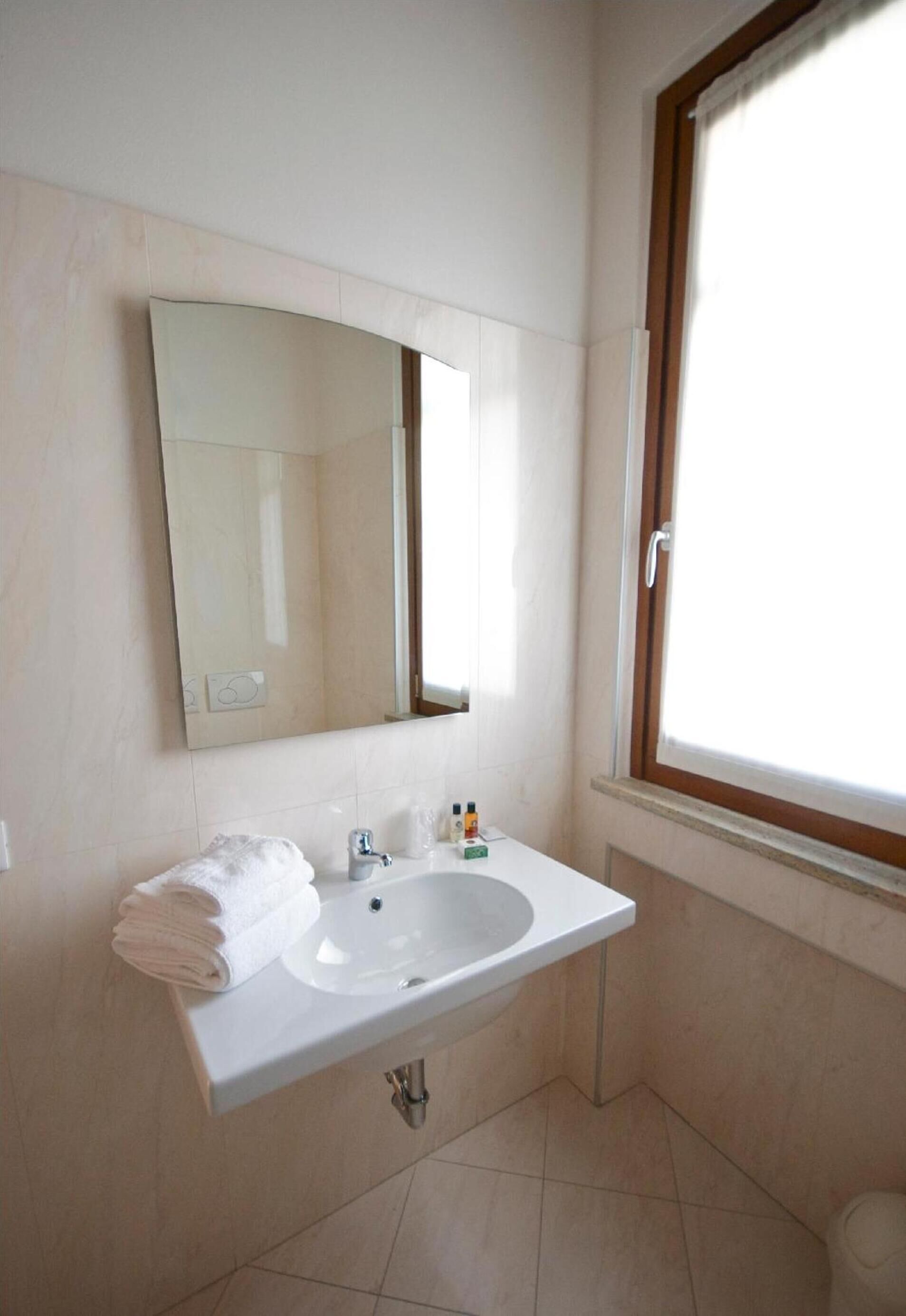 Une salle de bain avec un lavabo blanc, un miroir et une fenêtre.