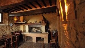 Una chimenea de piedra rústica con repisa de madera, rodeada de muros de piedra y vigas de madera.