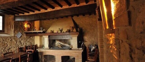 A rustic stone fireplace with a wooden mantel, surrounded by stone walls and wooden beams.