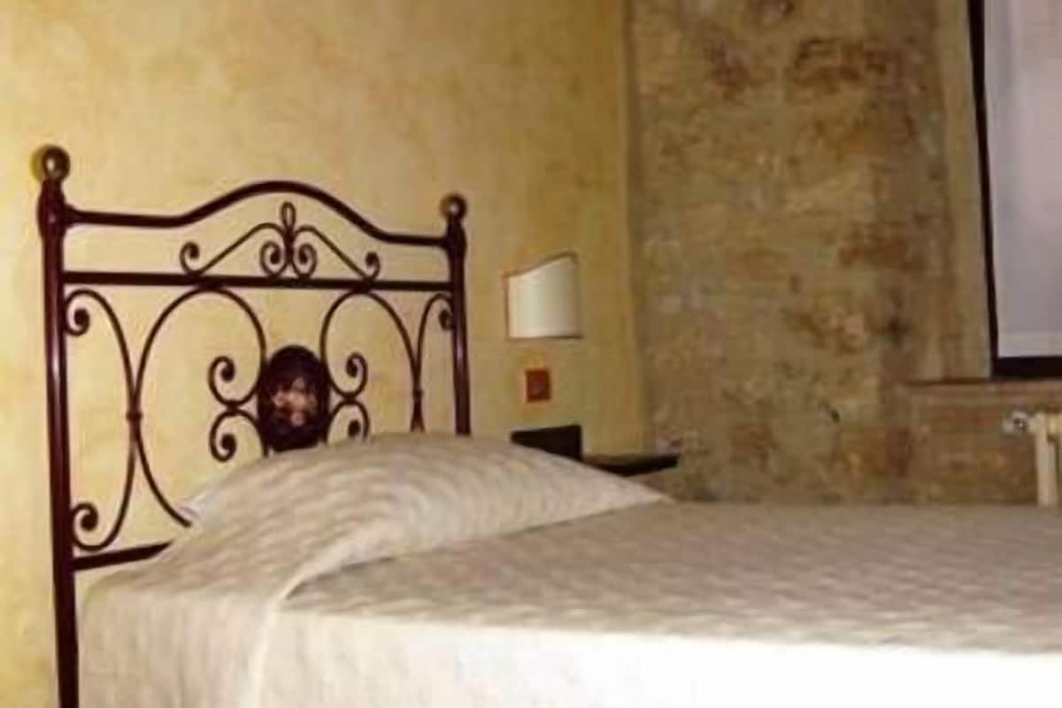 A single bed with a metal headboard in a room with stone walls and a window with curtains.