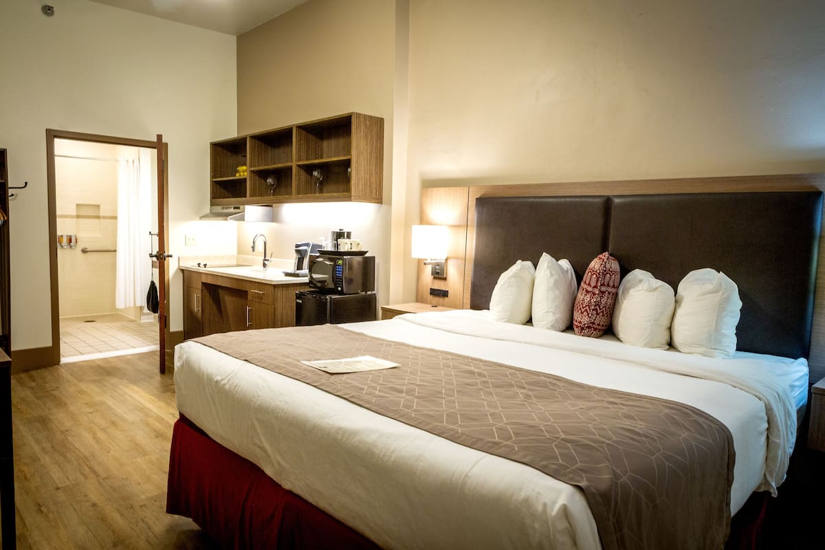 A hotel room with a large bed, a desk with a computer, a microwave, and a small sink.