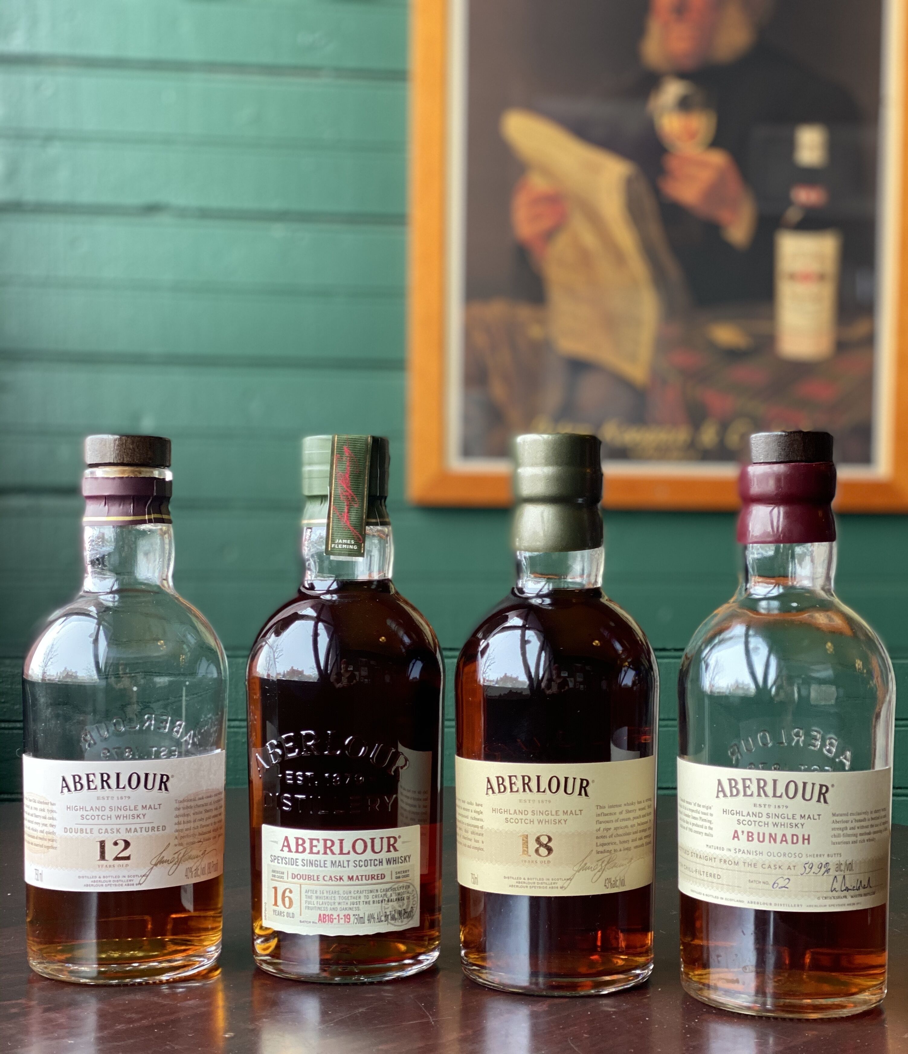 Four bottles of Aberlour whisky on a table with a green wall and a framed painting in the background.