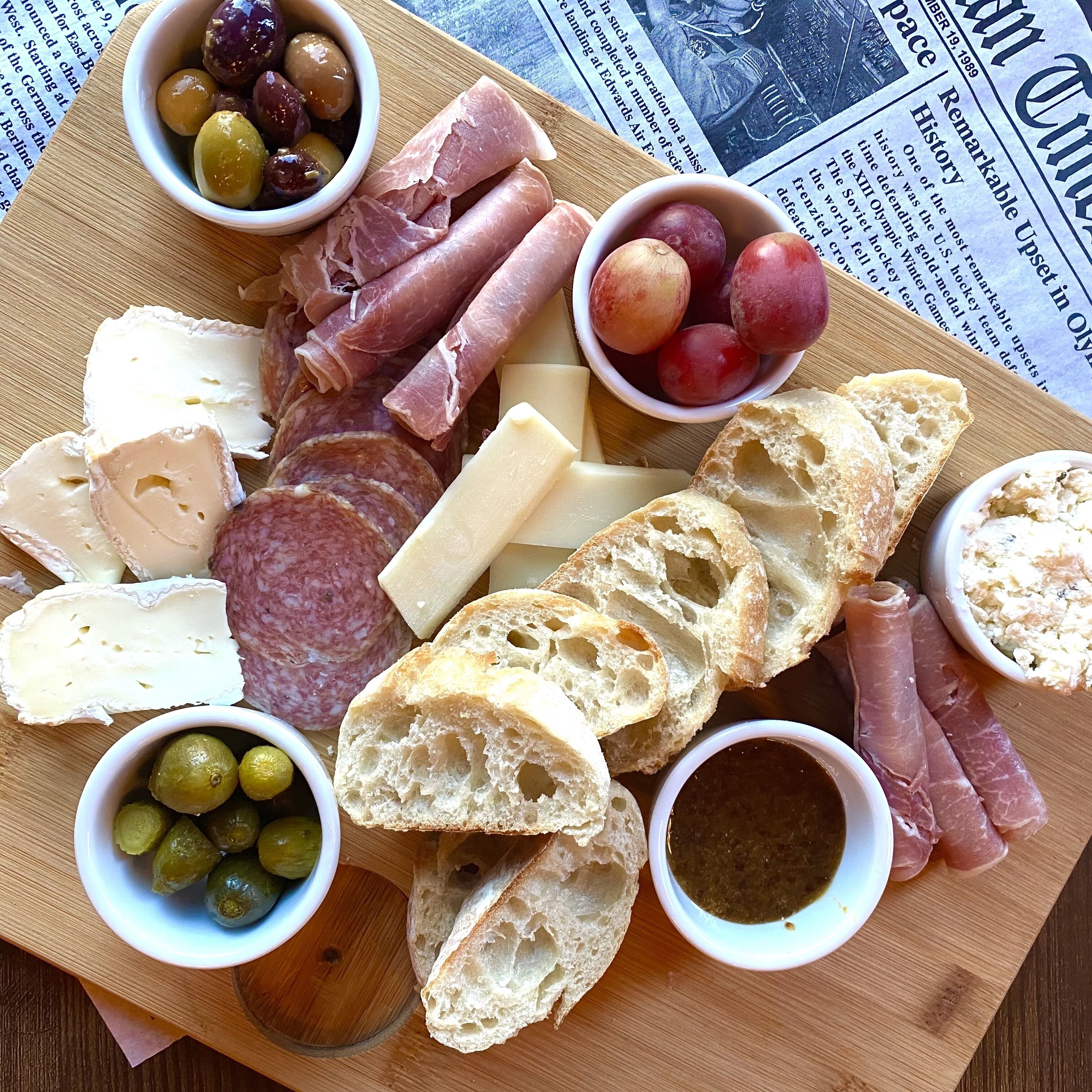 A charcuterie board with various meats, cheeses, olives, grapes, and bread.