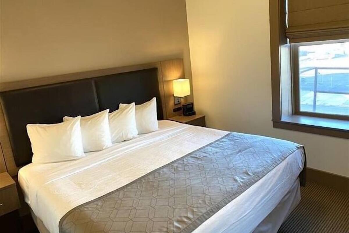 A hotel room with a large bed, a nightstand with a lamp, and a window with blinds.