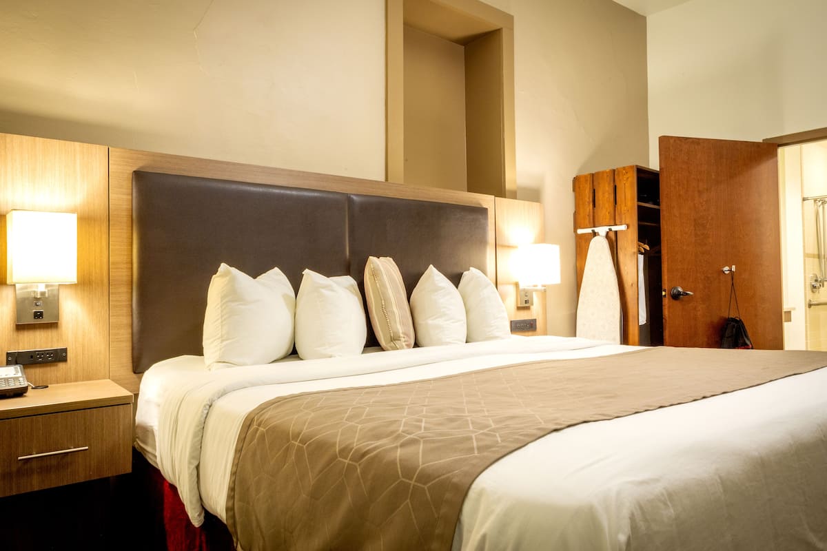 A hotel room with a large bed, two bedside tables, a wooden headboard, and a wardrobe.