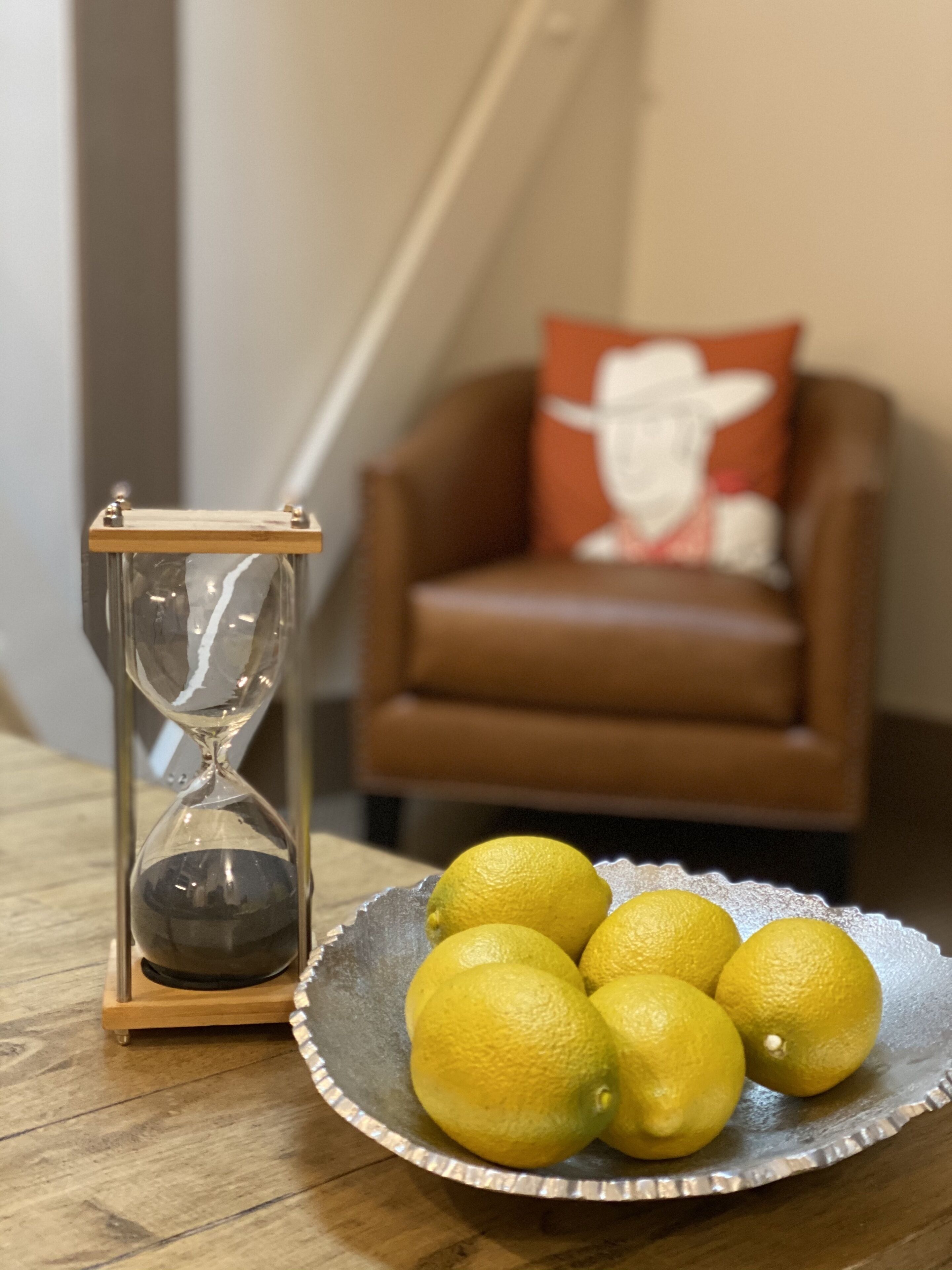 Un sablier et un bol de citrons sur une table en bois.