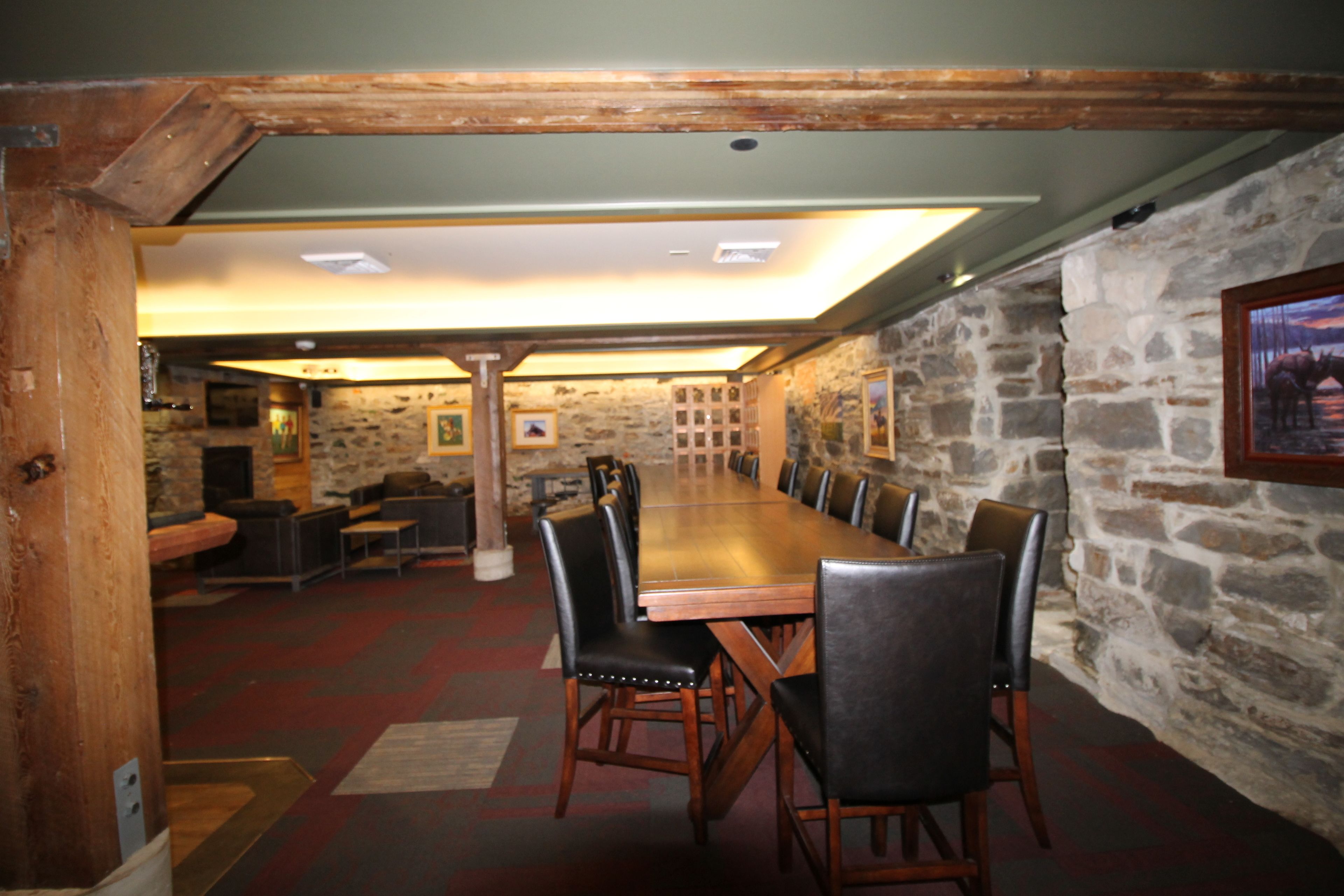 A conference room with a long wooden table and black leather chairs, stone walls, and a wooden ceiling.
