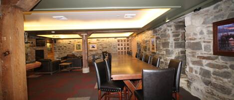 A conference room with a long wooden table and black leather chairs, stone walls, and a wooden ceiling.