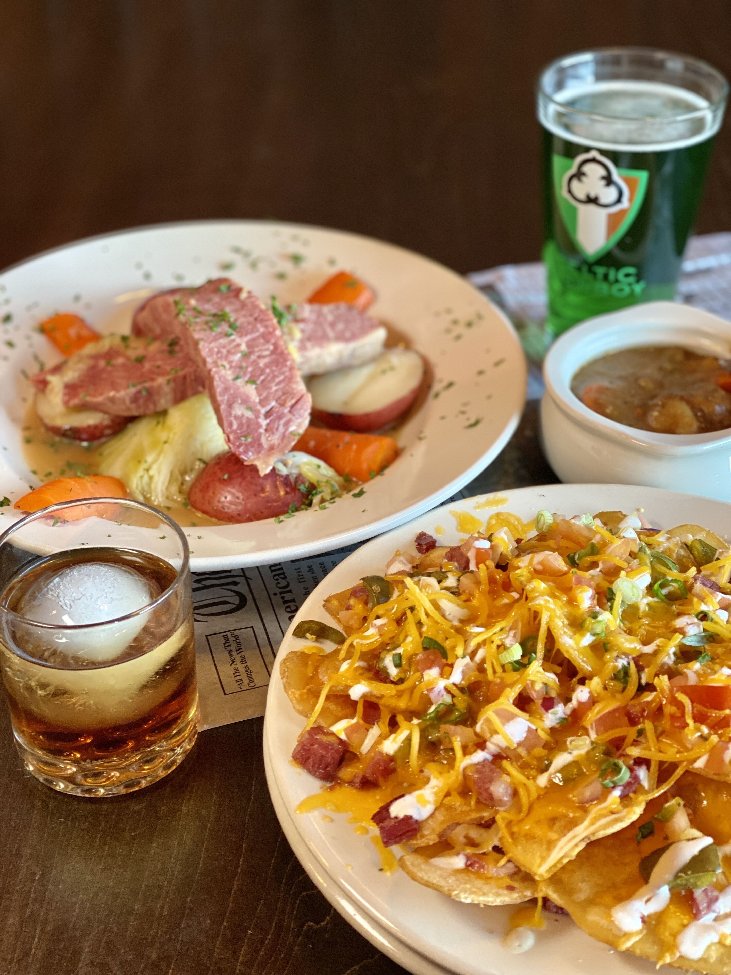 A meal with nachos, a soup bowl, and a glass of iced tea on a table.