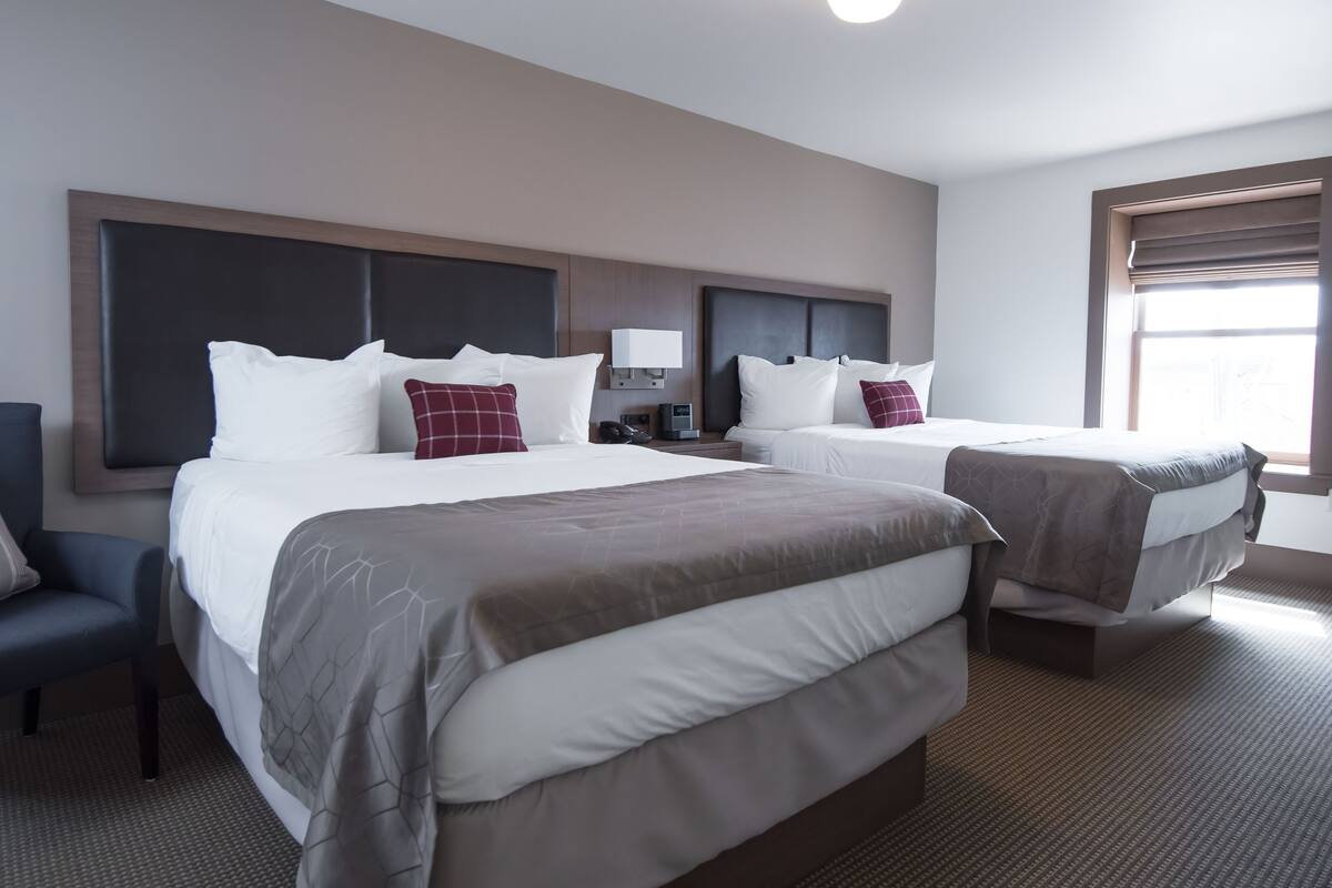A hotel room with two beds, a desk, a chair, and a window with blinds.