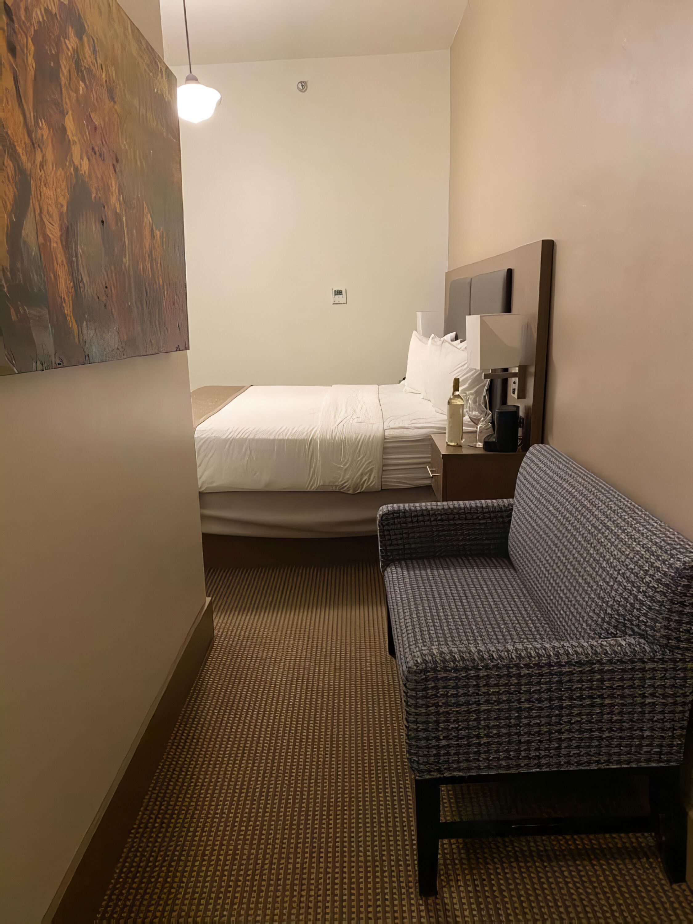 A hotel room with a bed, a sofa, a nightstand, a lamp, and a painting on the wall.
