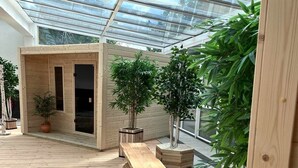 Une vaste terrasse en bois dotée d’un toit en verre, entourée de plantes en pot et agrémentée d’un banc en bois.