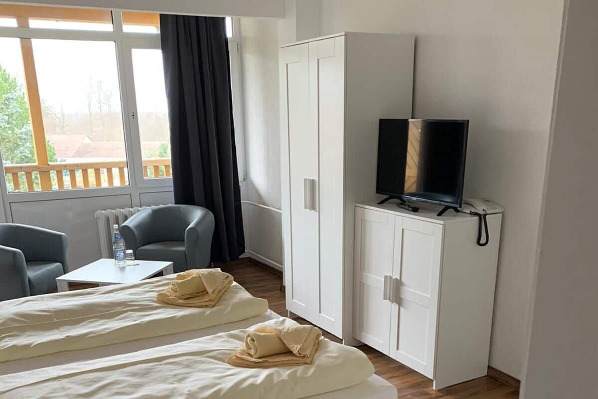 Une chambre d’hôtel avec deux lits, un téléviseur posé sur un meuble, un bureau avec une chaise et une fenêtre avec des rideaux.
