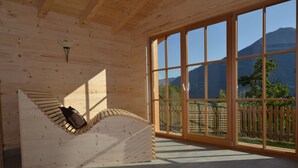 Un intérieur en bois, avec de grandes fenêtres, un banc en bois et une vue sur les montagnes.