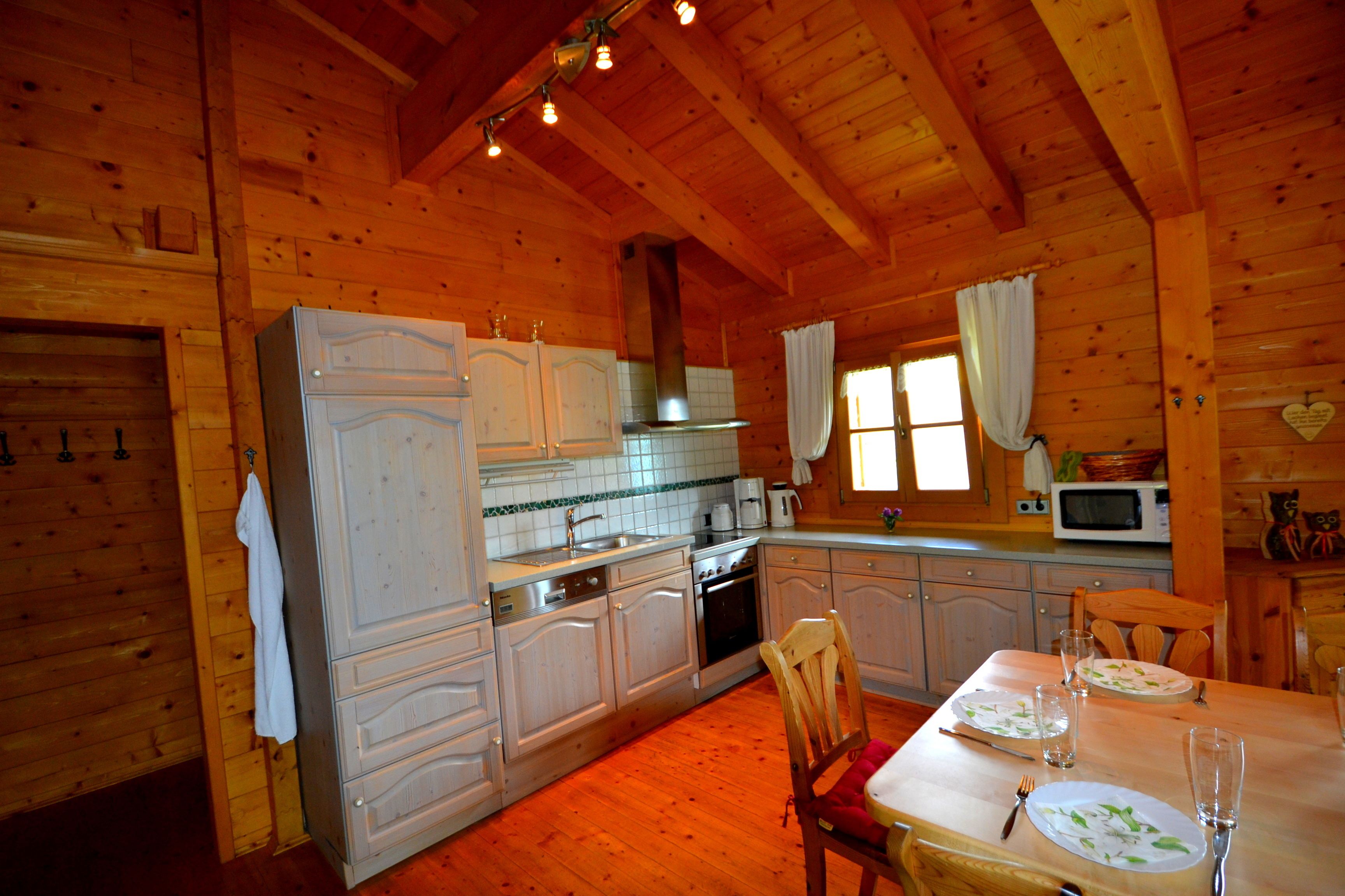 A wooden cabin kitchen with white cabinets, a dining table set for four, and a microwave.