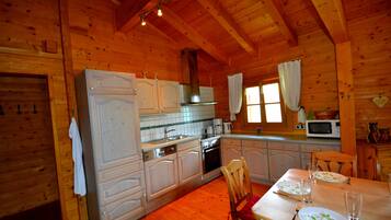 Cocina de cabaña de madera con armarios blancos, una mesa de comedor para cuatro personas y un microondas.