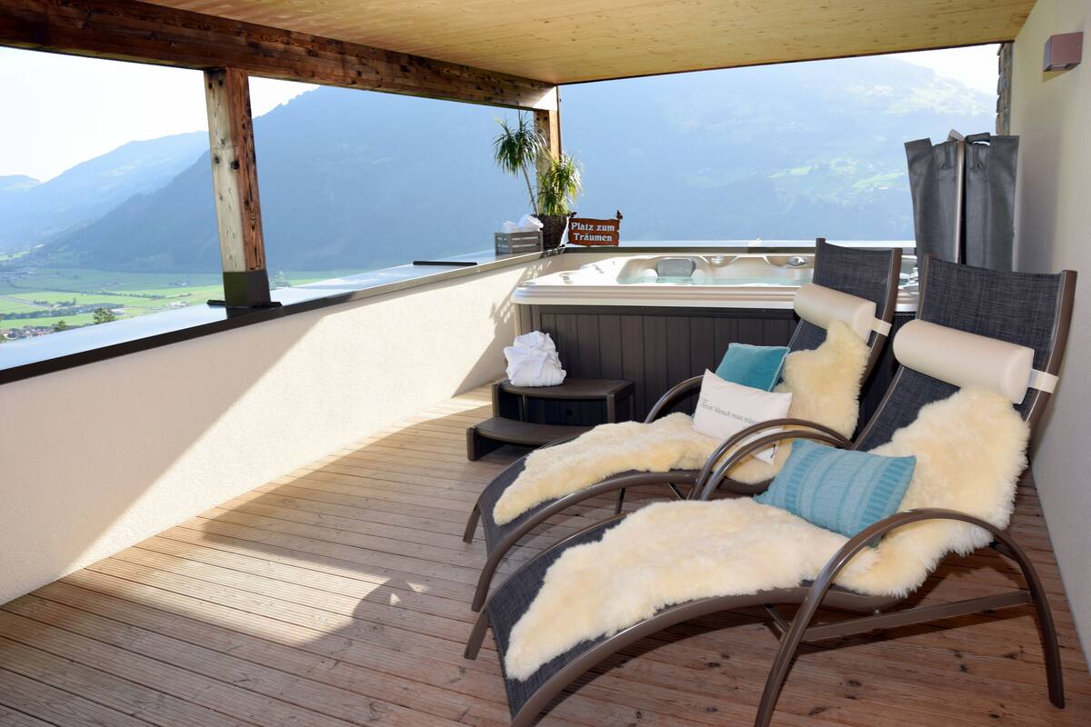 A balcony with two reclining chairs, a hot tub, and a view of mountains.