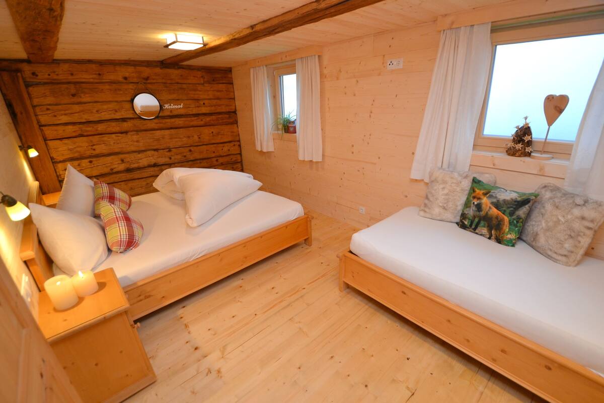 A cozy cabin with two wooden beds, a small window with curtains, and a mirror on the wall.