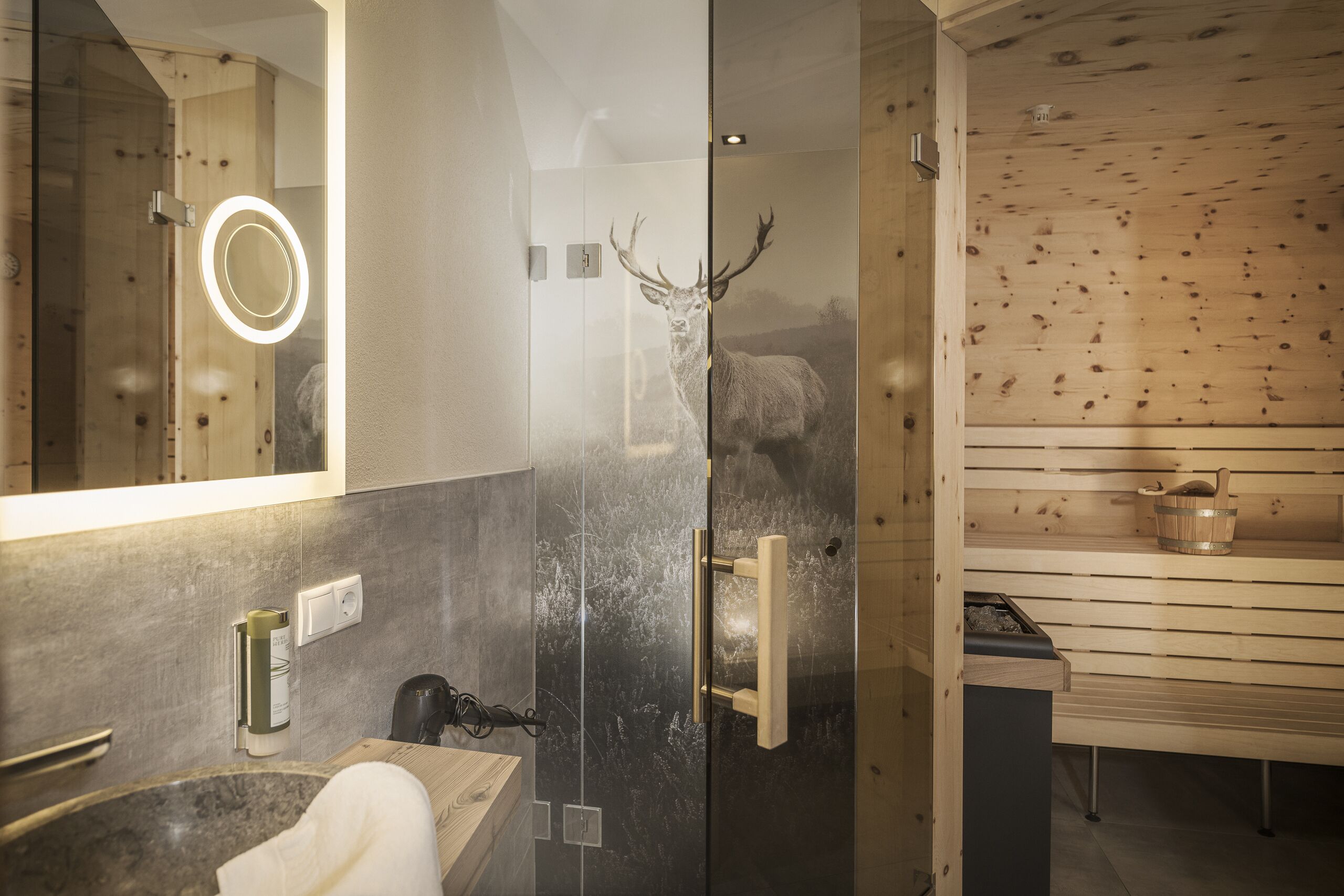Un baño moderno con cabina de ducha de vidrio, sauna de madera y espejo con luz.