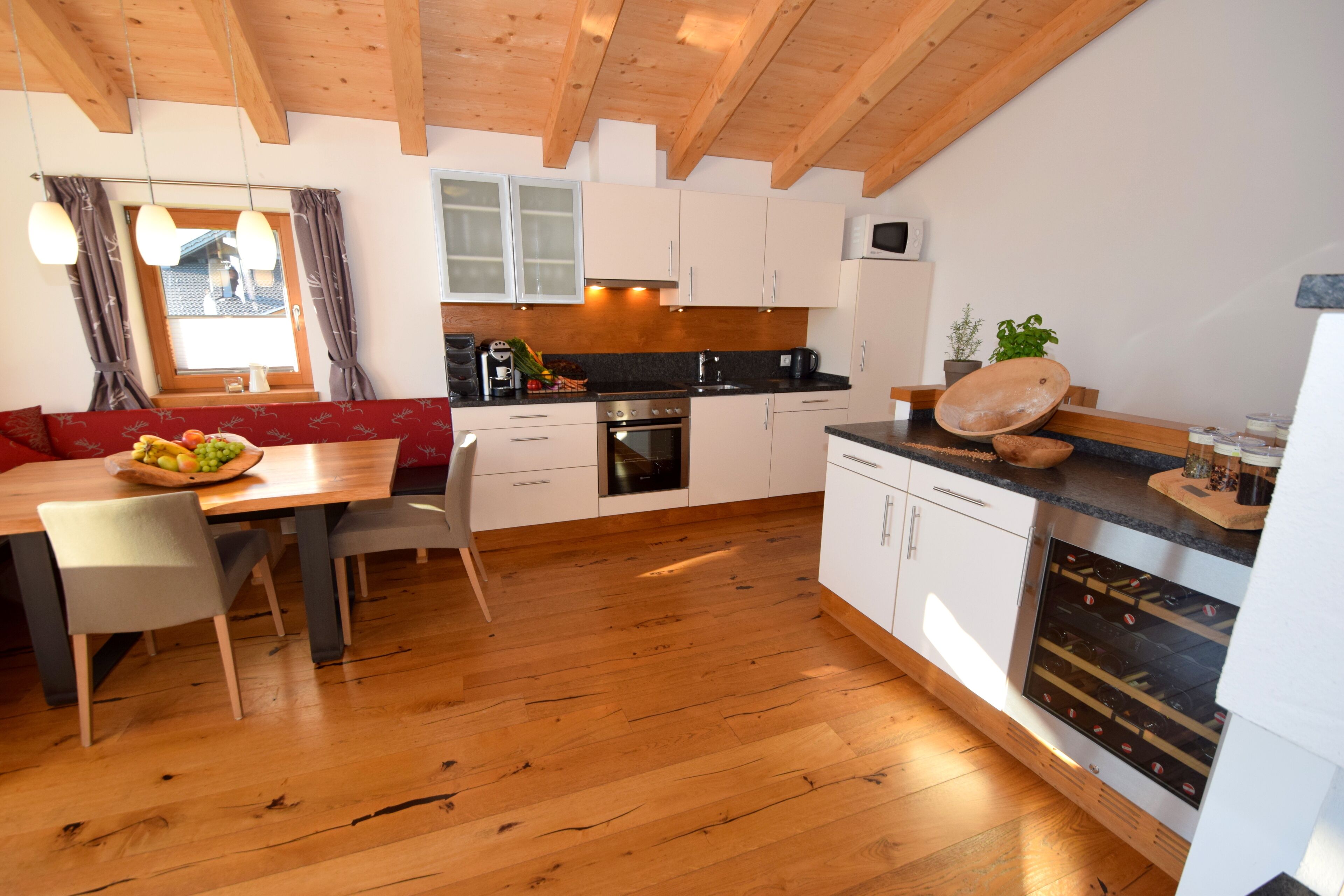 Une cuisine moderne avec un plancher en bois, des armoires blanches, un coin repas avec une table et des chaises, et un four encastré.