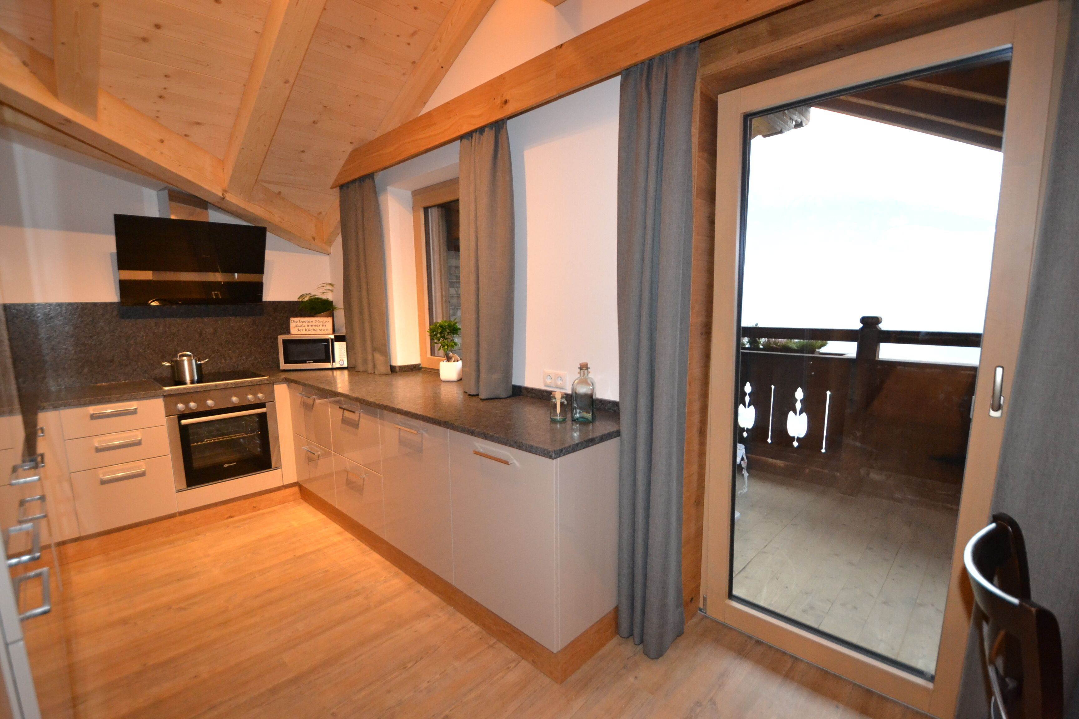 A modern kitchen with wooden beams, a built-in oven, a microwave, and a large sliding glass door leading to a balcony.