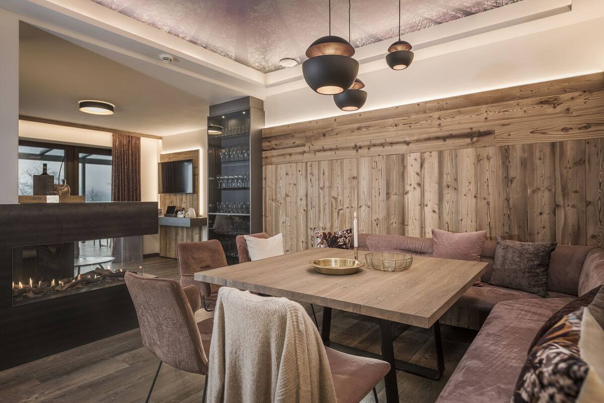A modern dining area with a wooden table, cushioned seating, pendant lighting, and a fireplace.