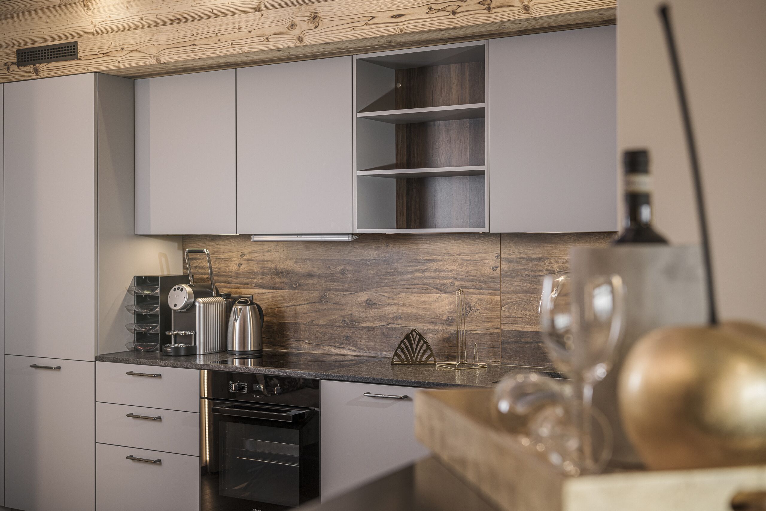 Cozinha moderna com armários cinzas, painel de madeira e eletrodomésticos de aço inoxidável.